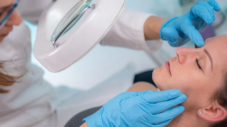 Dermatologo con guantes examinando piel del rostro de paciente con acné